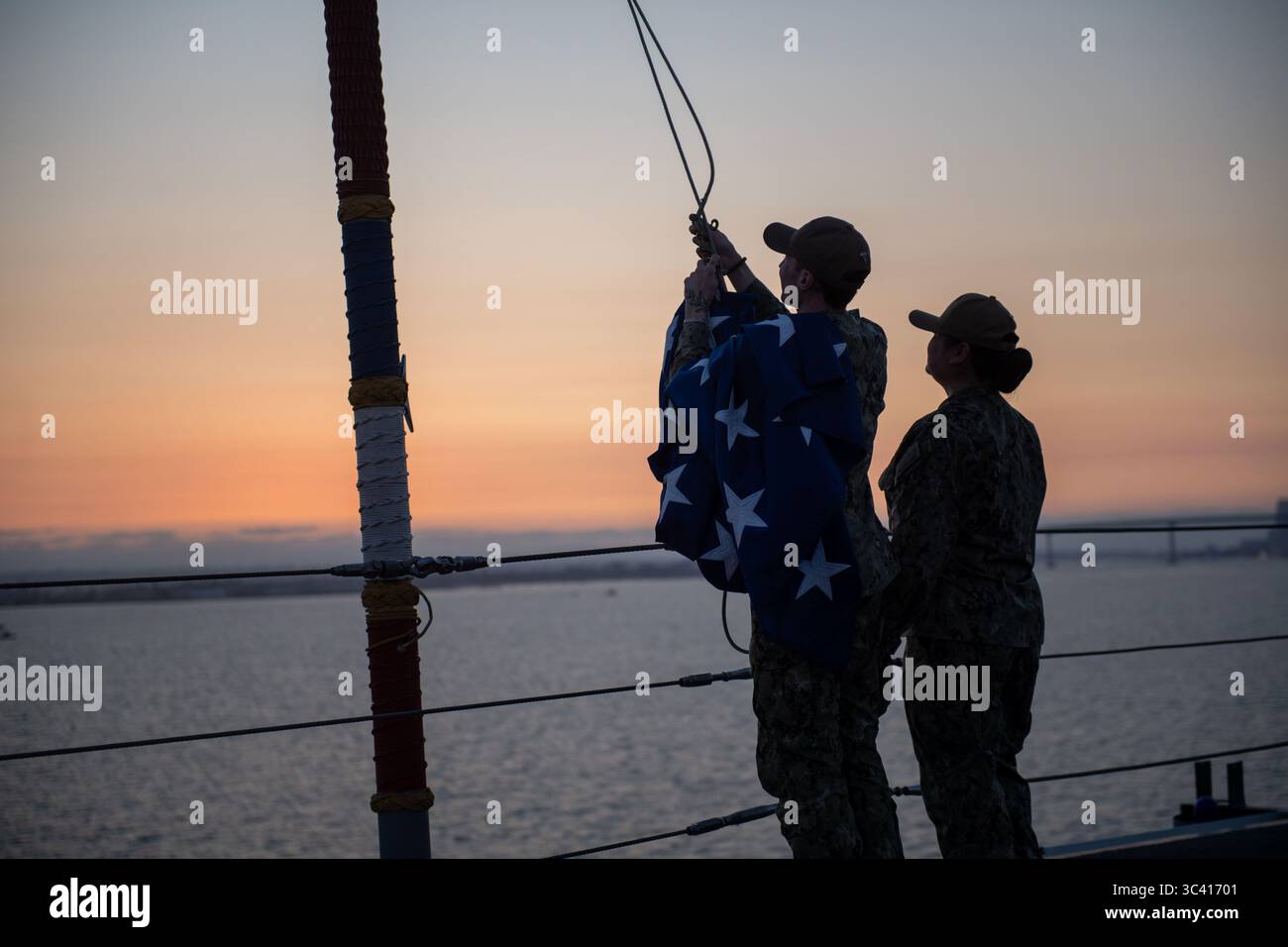 Hospital Corpsman 3nd Class, Evan Roy, Linke, gebürtige aus Jacksonville, North Carolina, und Hospital Corpsman 2nd Class, Nicole Singh, gebürtige aus Phoenix, Arizona, beide der USS Boxer (LHD 4) zugeteilt, senkt die Union Jack an Bord von Boxer, 4. Juli 2025. Boxer ist ein amphibisches Angriffsschiff der Wasp-Klasse, das derzeit auf der Marinebasis San Diego stationiert ist. (Foto der US Navy von Seaman Dustin Drake) Stockfoto