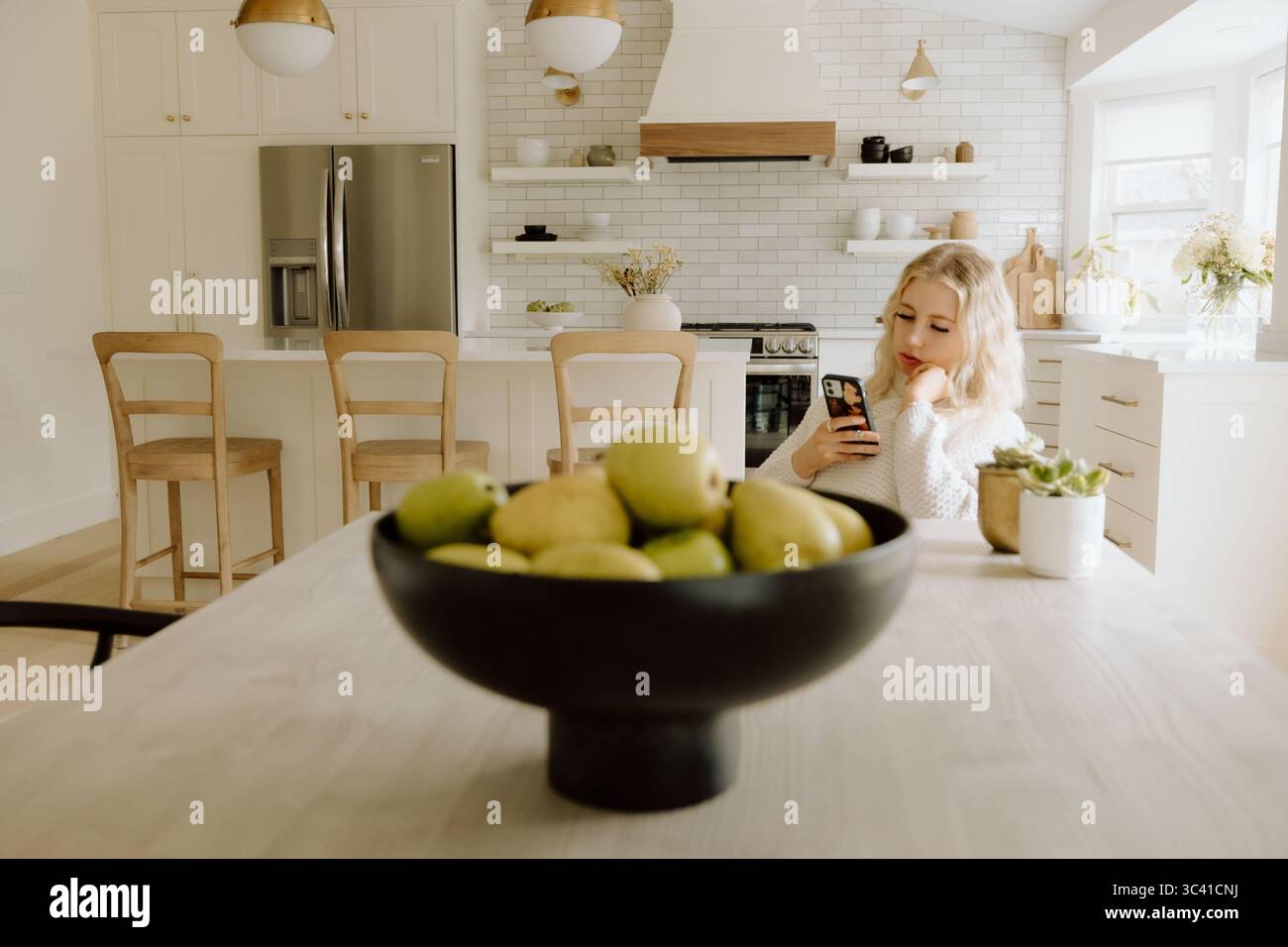 Frau mit Smartphone in der Küche in der Nähe einer Schüssel frischer Birnen Stockfoto