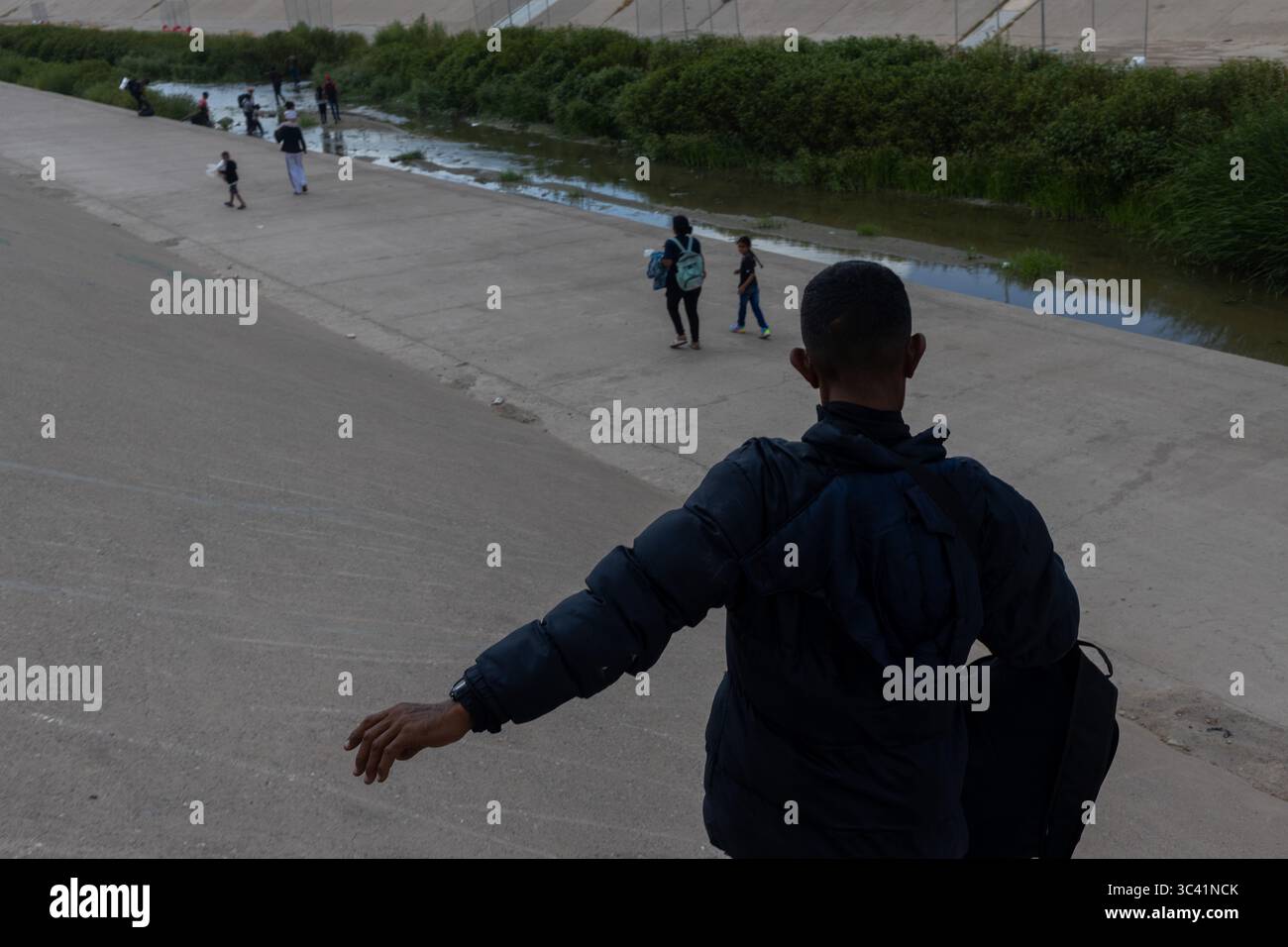 Der Mensch beobachtet Migranten entlang des Ciudad Juarez-Kanals und spiegelt Migrationsherausforderungen wider. Stockfoto
