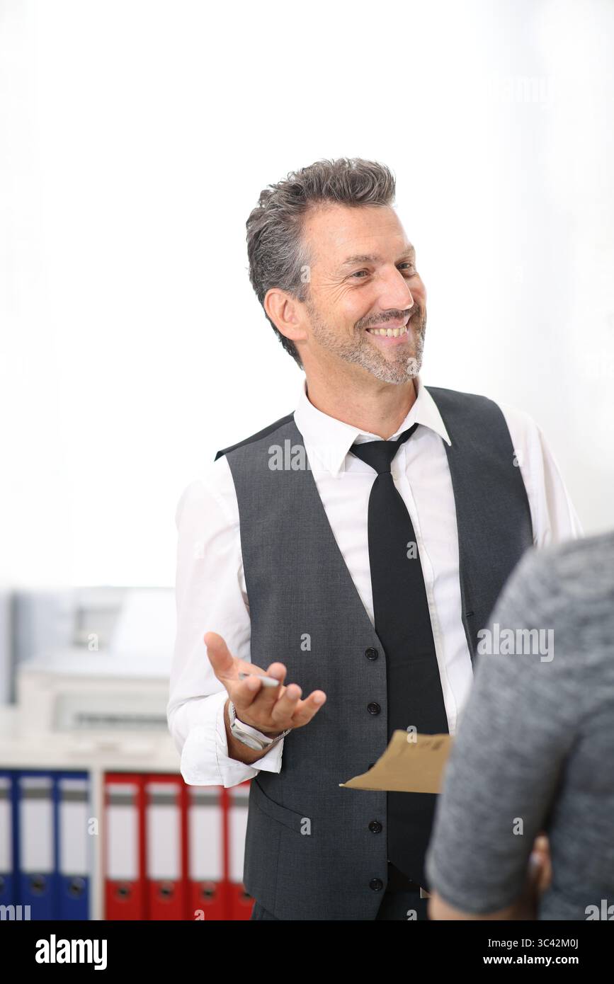 Mann im Anzug, der mit der Frau im Büro spricht, lächelt Stockfoto