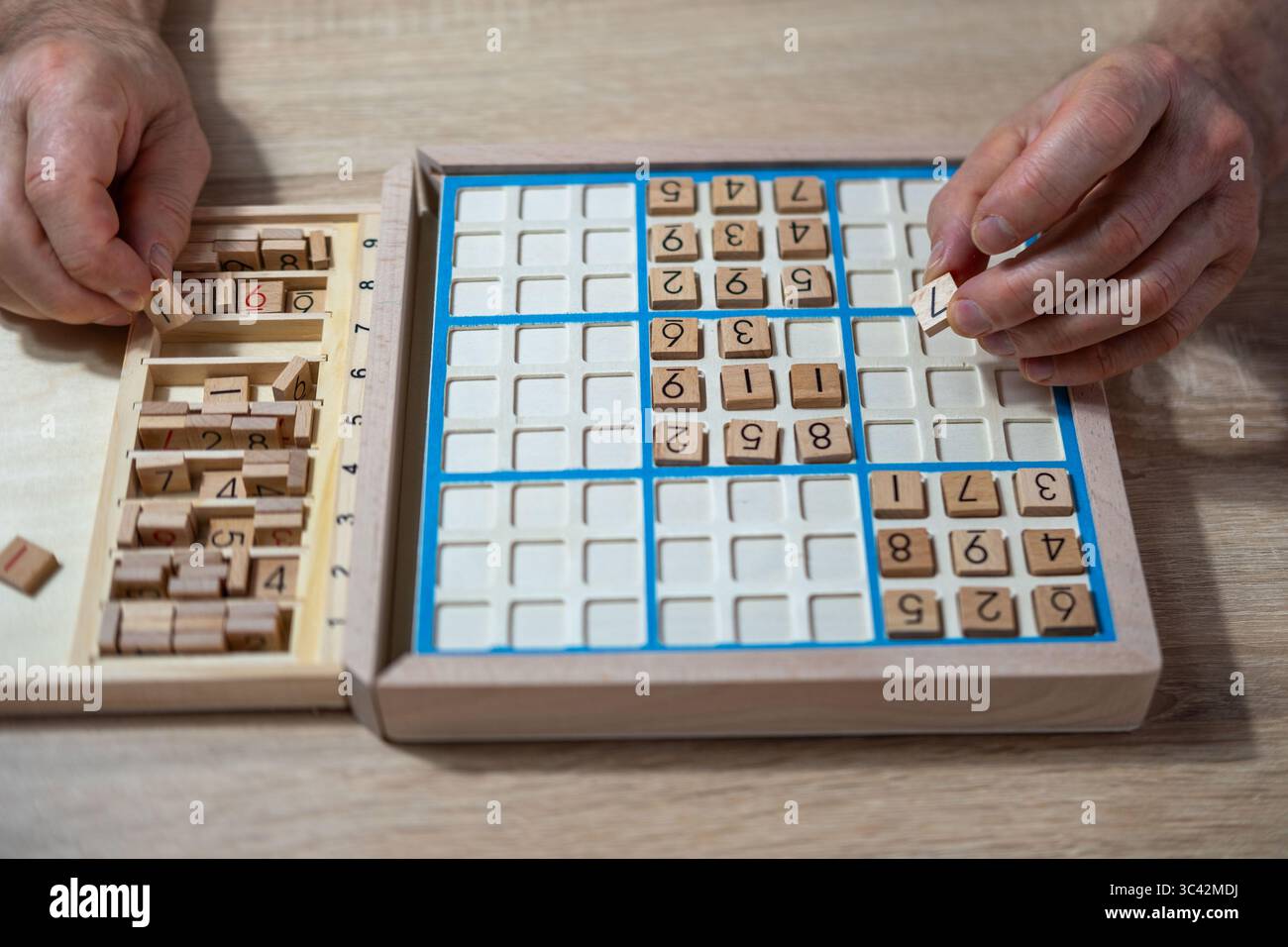 Close-up-Hände sorgsam die Nummer in das Sudoku-Puzzle legen, eine ältere Person, die tief in das Lösen von herausfordernden Rätseln, mentaler Stimulation und Enjo vertieft ist Stockfoto