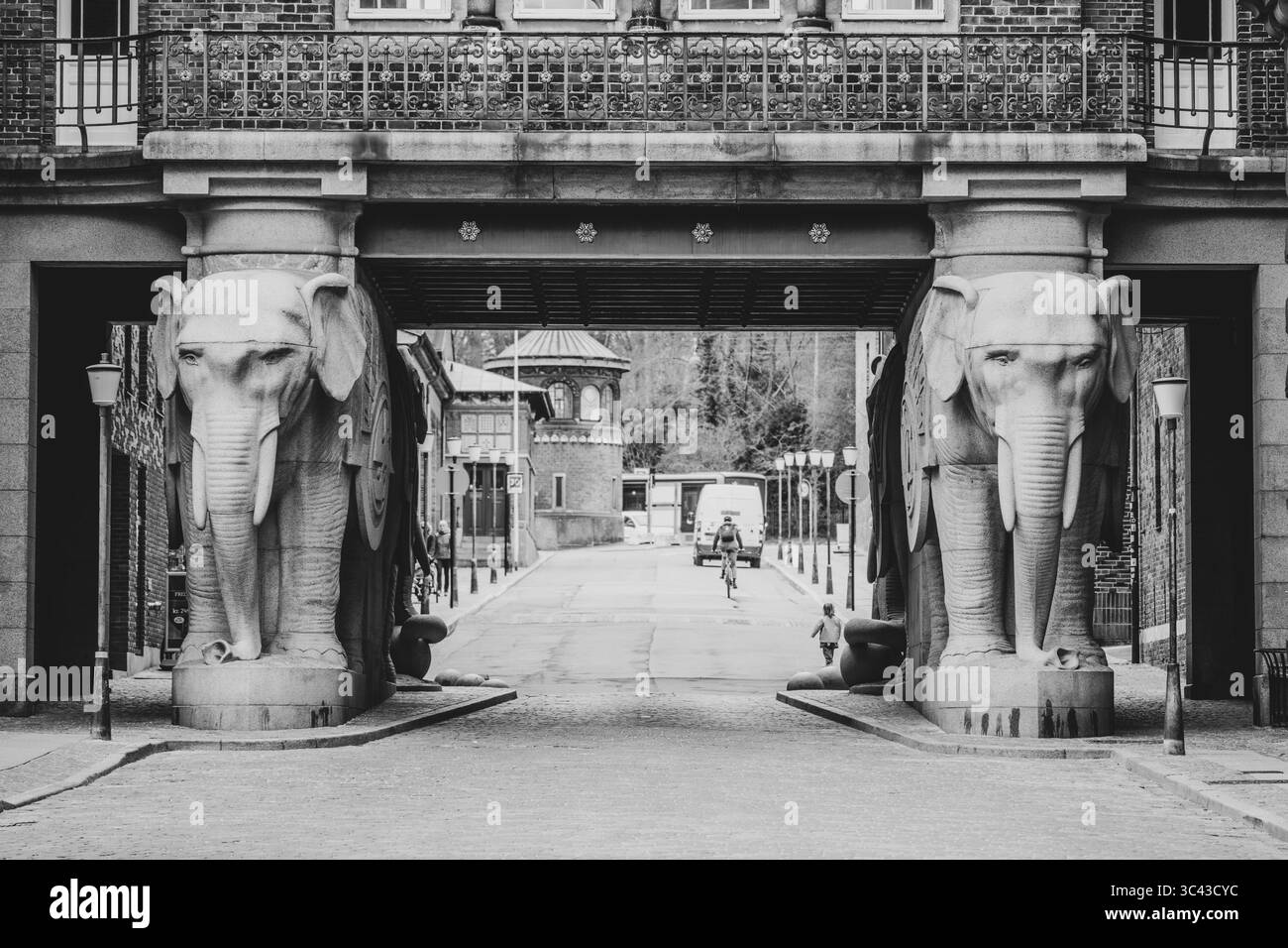 Elefantenskulpturen stehen am Eingang einer Brauerei in Kopenhagen, Dänemark. An einem ruhigen Tag fährt ein Fußgänger mit dem Fahrrad unter der beeindruckenden Struktur. Stockfoto