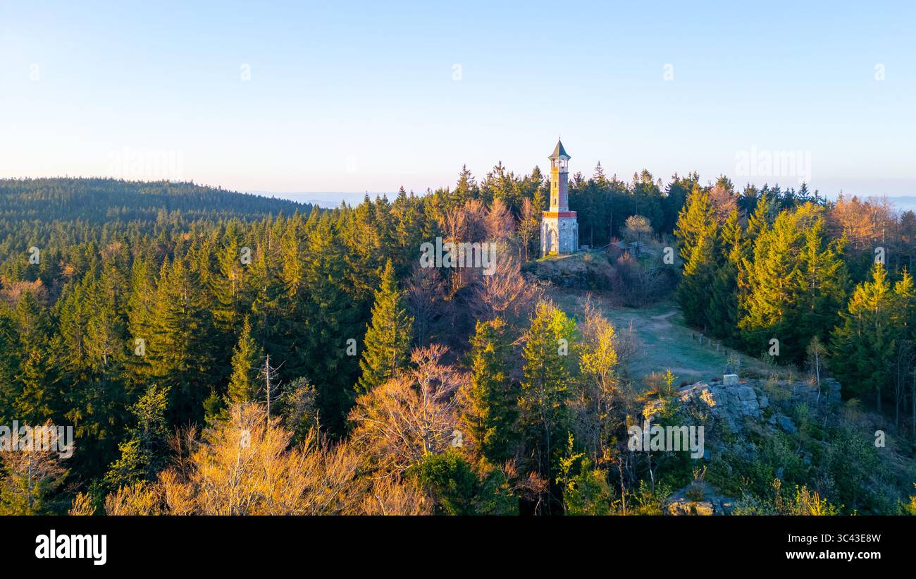 An einem sonnigen Frühlingsmorgen erhebt sich der Stepanka Aussichtsturm majestätisch auf den grünen Hügeln in Korenov, umgeben von üppigen Wäldern und einem klaren blauen Himmel. Stockfoto
