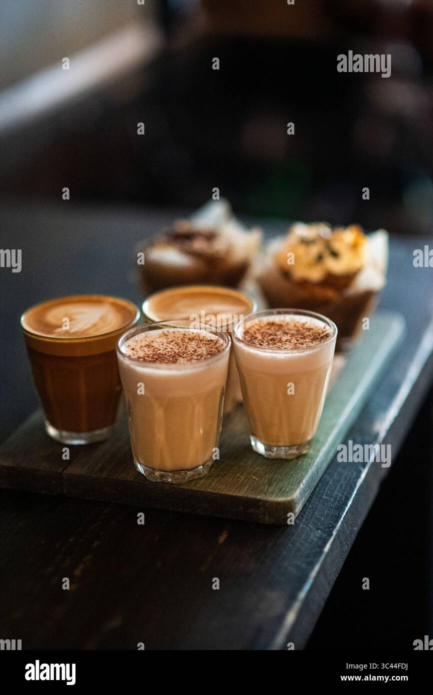 Vier Tassen mit einer Vielzahl von Kaffeegetränken und heißer Schokolade auf einer Cafetreske. Eine gemütliche und einladende Coffee-Shop-Szene, in der sich verschiedene Wärme zeigt. Stockfoto