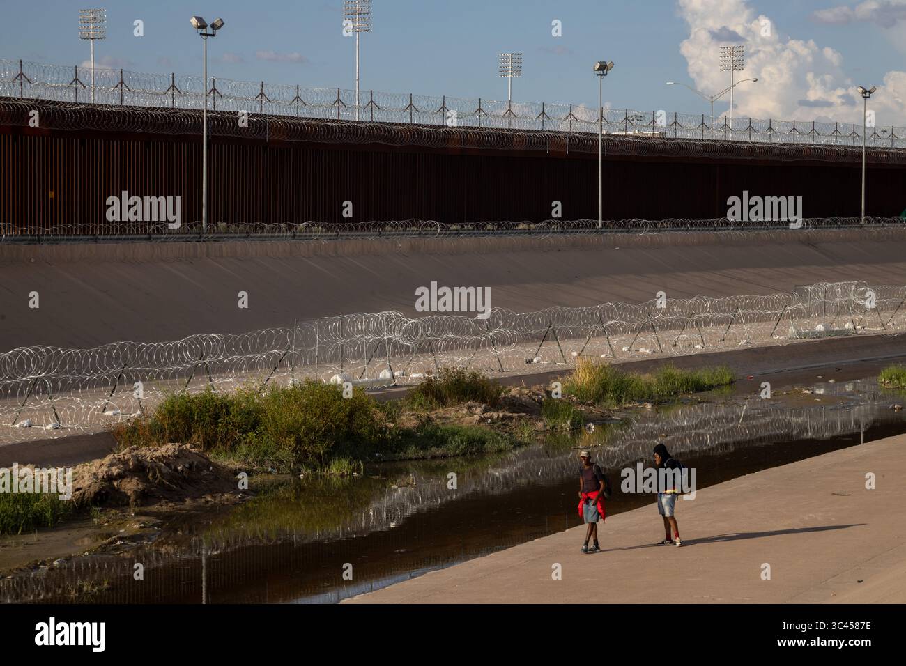 Zwei Menschen gehen am befestigten Grenzzaun Ciudad Juarez vorbei, ein deutliches Symbol für Migrationsherausforderungen. Stockfoto