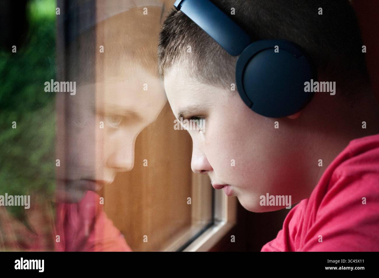 Junge, der Musik über Kopfhörer hört und aus dem Fenster blickt Stockfoto