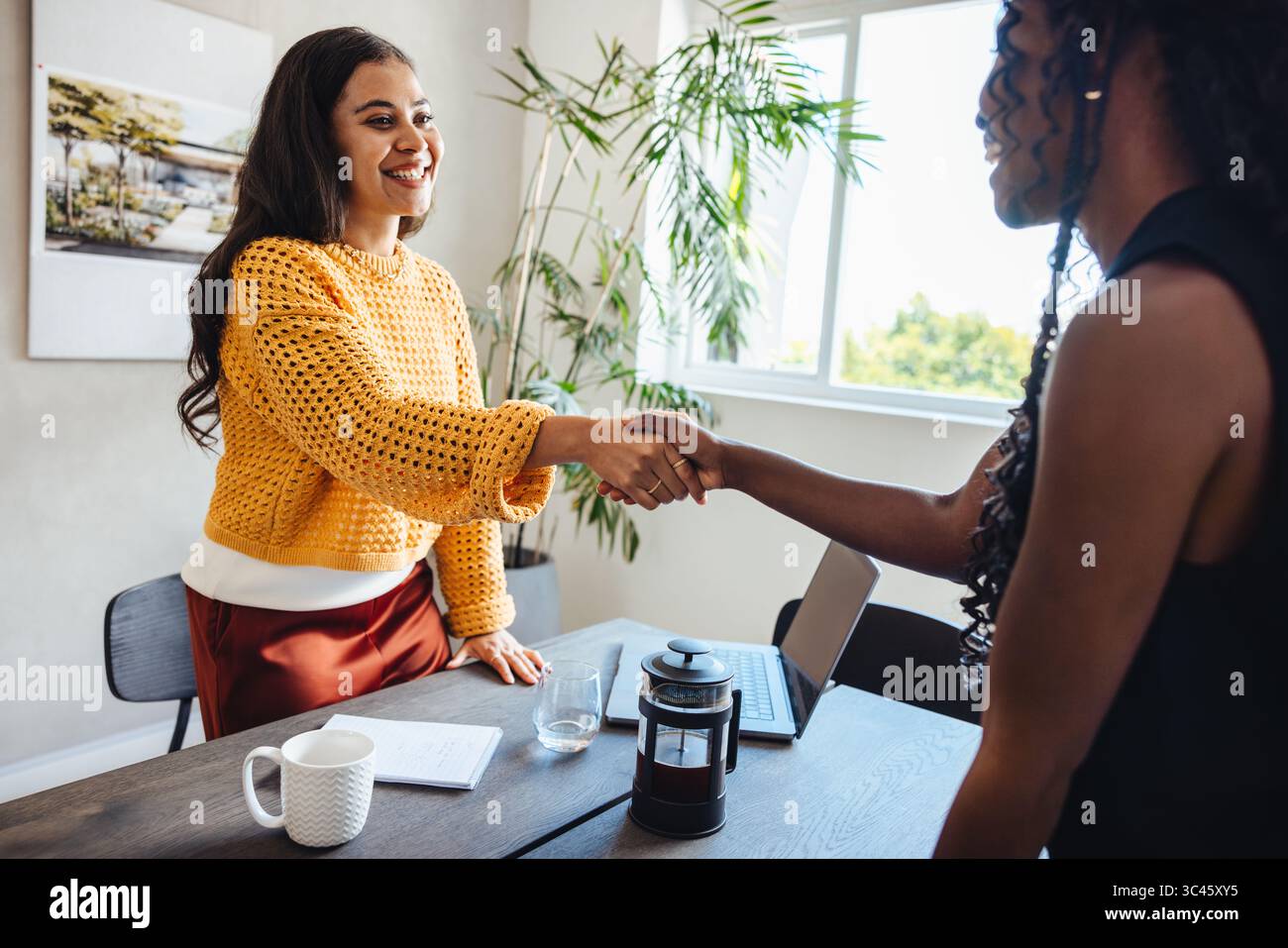 Zwei professionelle Frauen in ihren dreißiger Jahren, die bei einem Treffen in einem Architekturstudio die Hände schütteln, symbolisieren Zusammenarbeit, Respekt Stockfoto