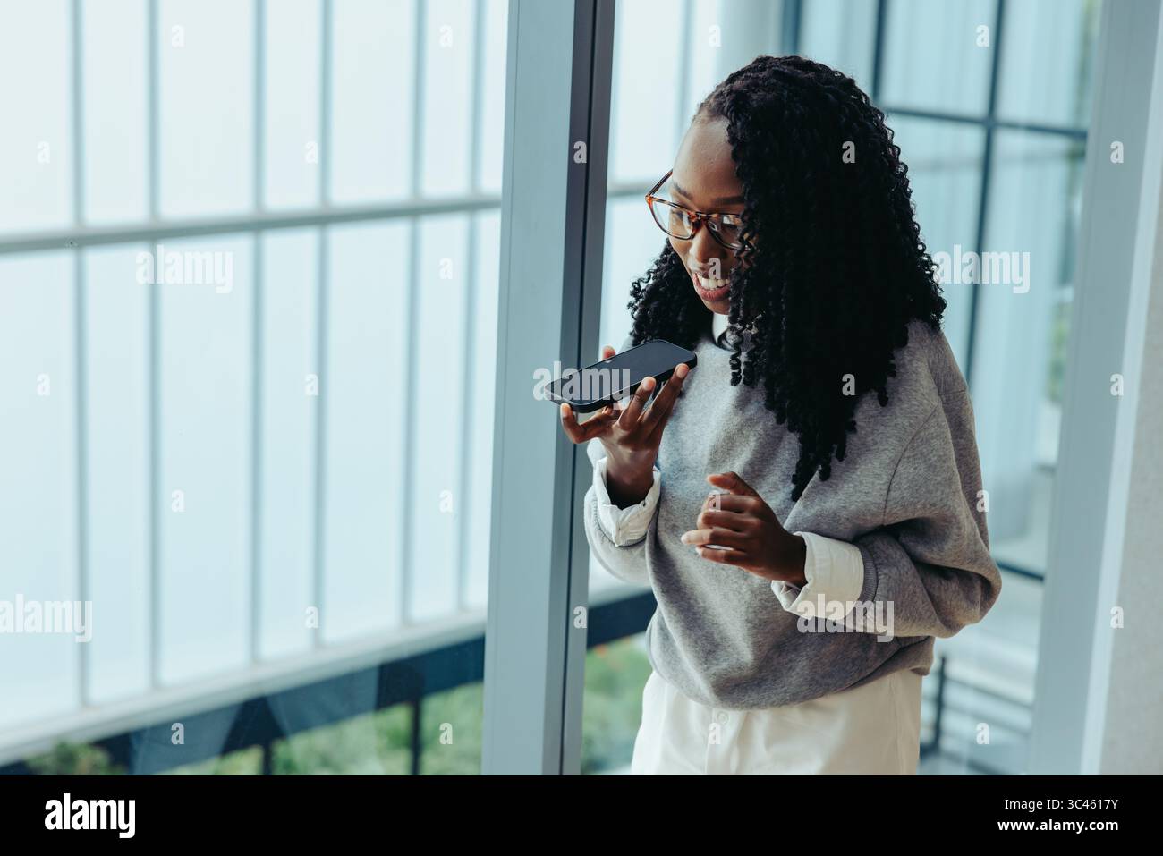Eine selbstbewusste Frau nutzt ihr Telefon, um in einer modernen Büroumgebung zu kommunizieren und unterstreicht die Bedeutung von Technologie im Unternehmen Stockfoto