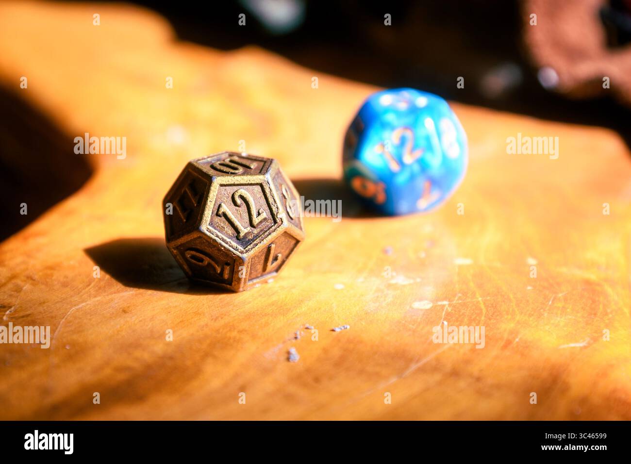 Metallische und blaue D12-Matrizen sitzen auf einer polierten Holzoberfläche in warmem natürlichem Licht. Stockfoto