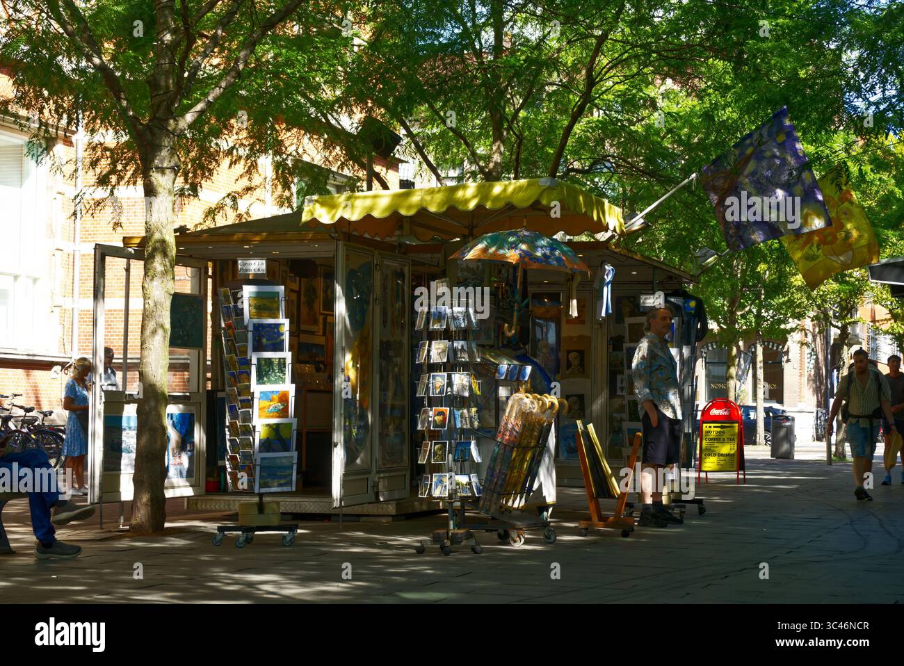 Amsterdam, niederlande, 12. juli 2025, Inhaber eines kleinen Unternehmens, der an einem sonnigen Sommertag in A an einem Souvenirkiosk Postkarten, Regenschirme und Kunstdrucke verkauft Stockfoto
