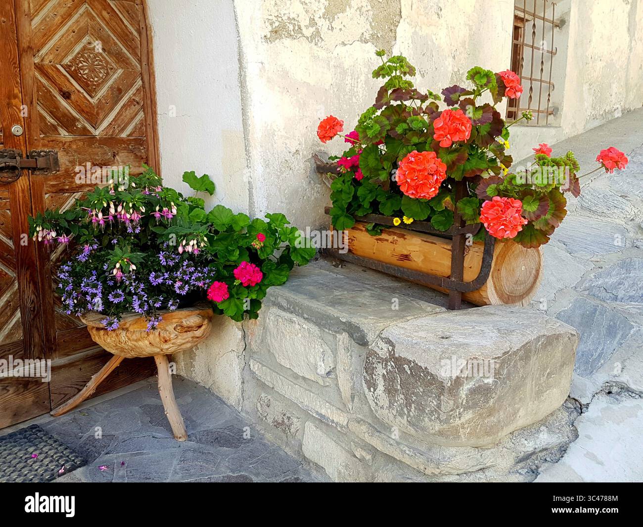 Traditionelle Engadiner Holztür mit Schnitzereien und rustikalen Blumendekorationen in Holztöpfen Stockfoto