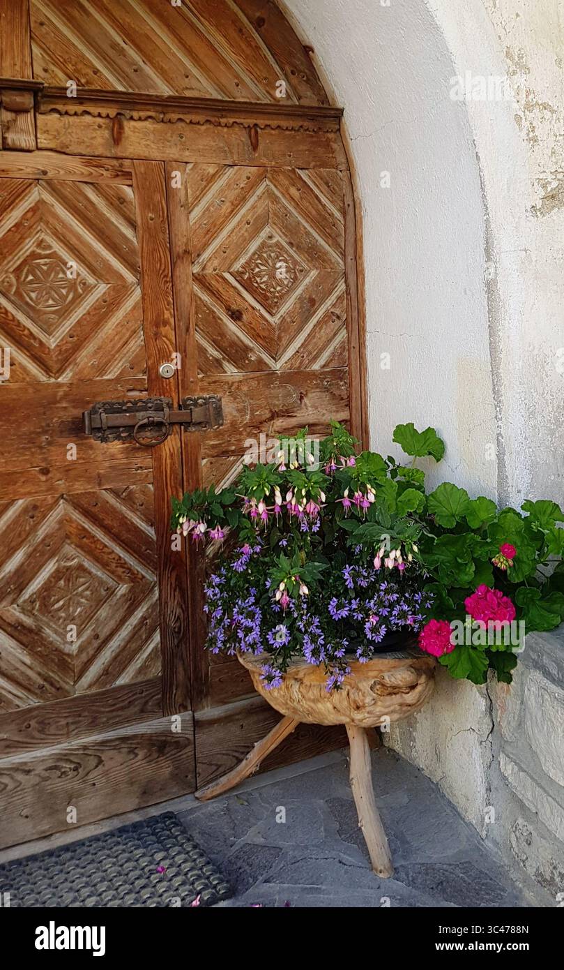 Traditionelle Engadiner Holztür mit Schnitzereien und rustikalen Blumendekorationen in Holztöpfen Stockfoto