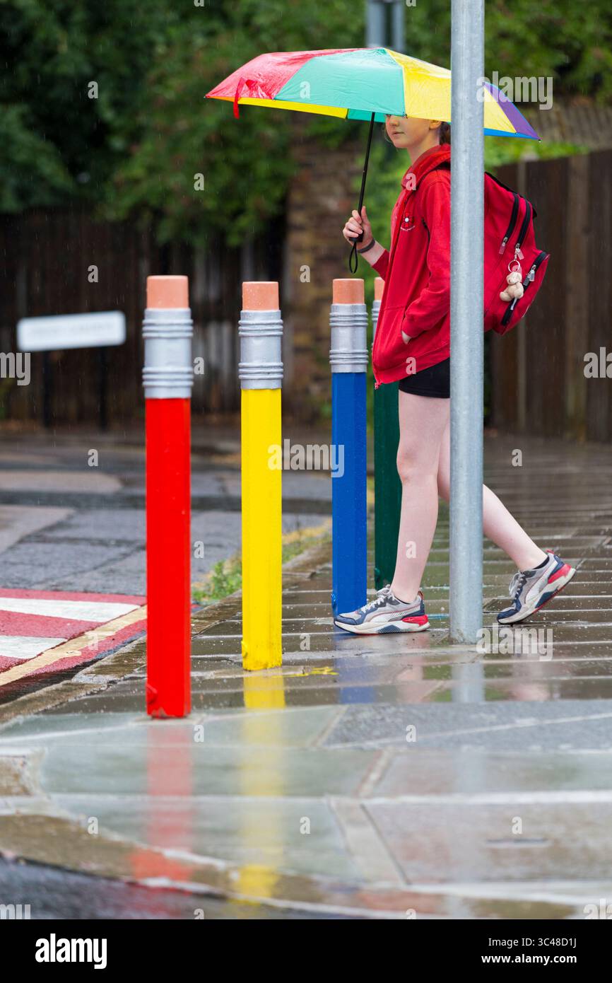 11-jähriges Mädchen/Schüler überquert die Straße/Straße mit farbigen Verkehrspollern in Form von Bleistift/Bleistiften. Twickenham. London. UK. (145). Stockfoto