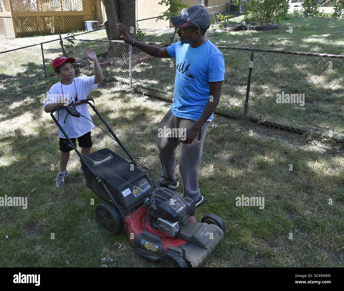 10. Juli 2018 – USA – Rodney Smith, Right, aus Huntsville, Ala., gibt Erron Blockmon, 9, von Lee's Summit, Kan., nachdem sie am Dienstag Nachmittag, den 10. Juli 2018, im Overland Park, Kan, einen Rasen gemäht haben. Smith hat sich zum Ziel gesetzt, Rasenmähen für ältere Menschen, Veteranen oder alleinstehende Mütter in allen 50 bundesstaaten zu unterstützen. Er nennt seine Bemühungen: "Einen Rasen nach dem anderen verändern". Smith hat nach seinem Aufenthalt in Kansas nur noch vier weitere bundesstaaten. (Kreditbild: © Rich Sugg/TNS via ZUMA Wire) Stockfoto