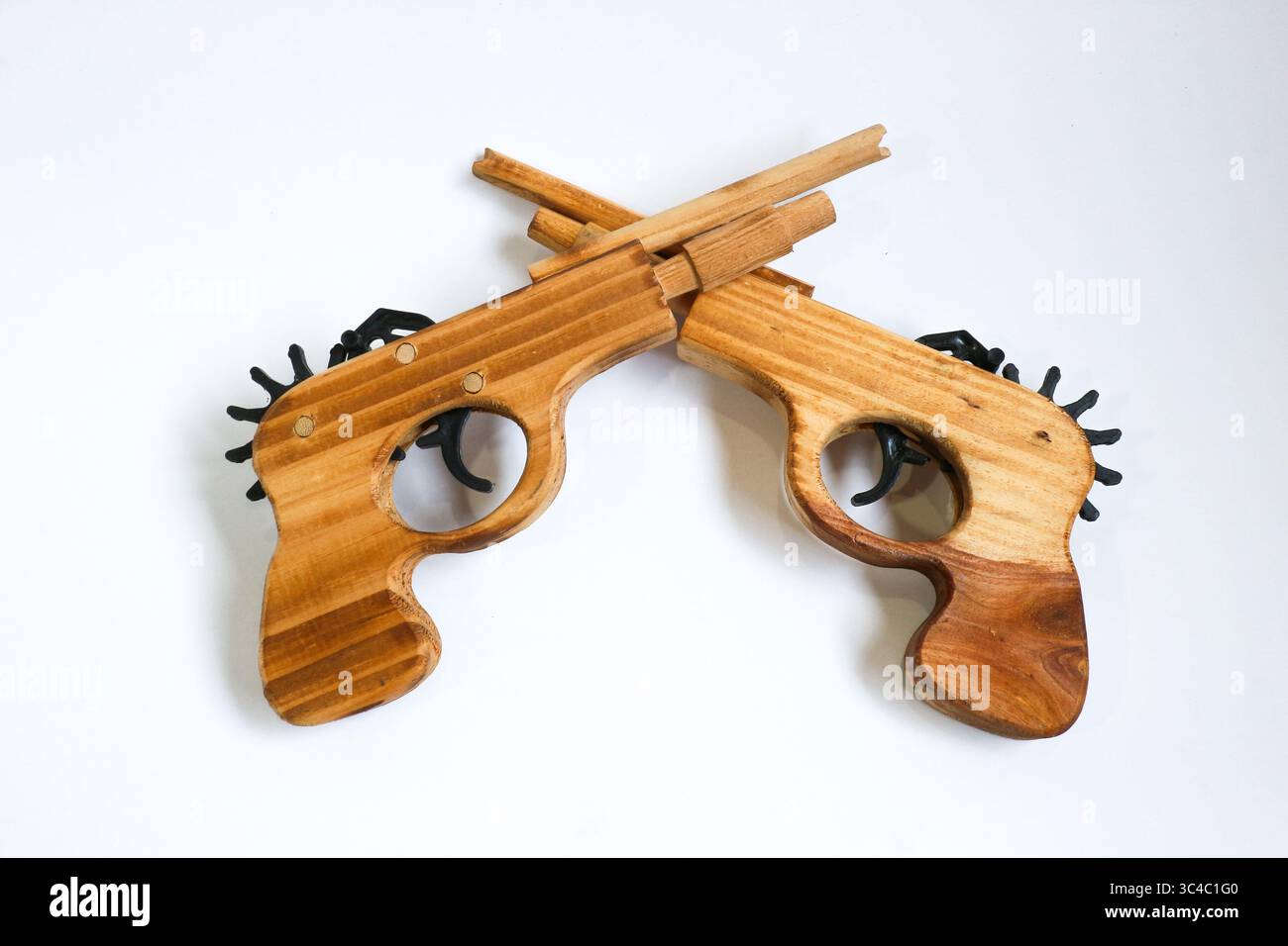 Zwei handgefertigte Holzpistolen mit unterschiedlichen Kornmustern, die in X-Form kreuzt sind. Fotografiert auf weißem Hintergrund symbolische und künstlerische Komposition. Stockfoto
