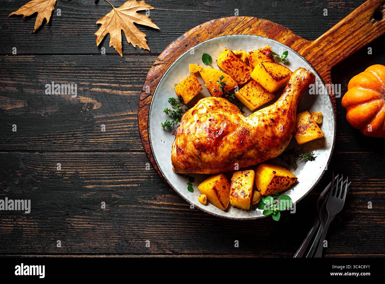 Saisonale Herbstmahlzeit: Gebratenes Hähnchenviertel und Kürbis mit Knoblauch und Kräutern auf Holztisch mit Ahornblättern und Kürbissen, Kopierraum. Im Ofen gebacken Stockfoto