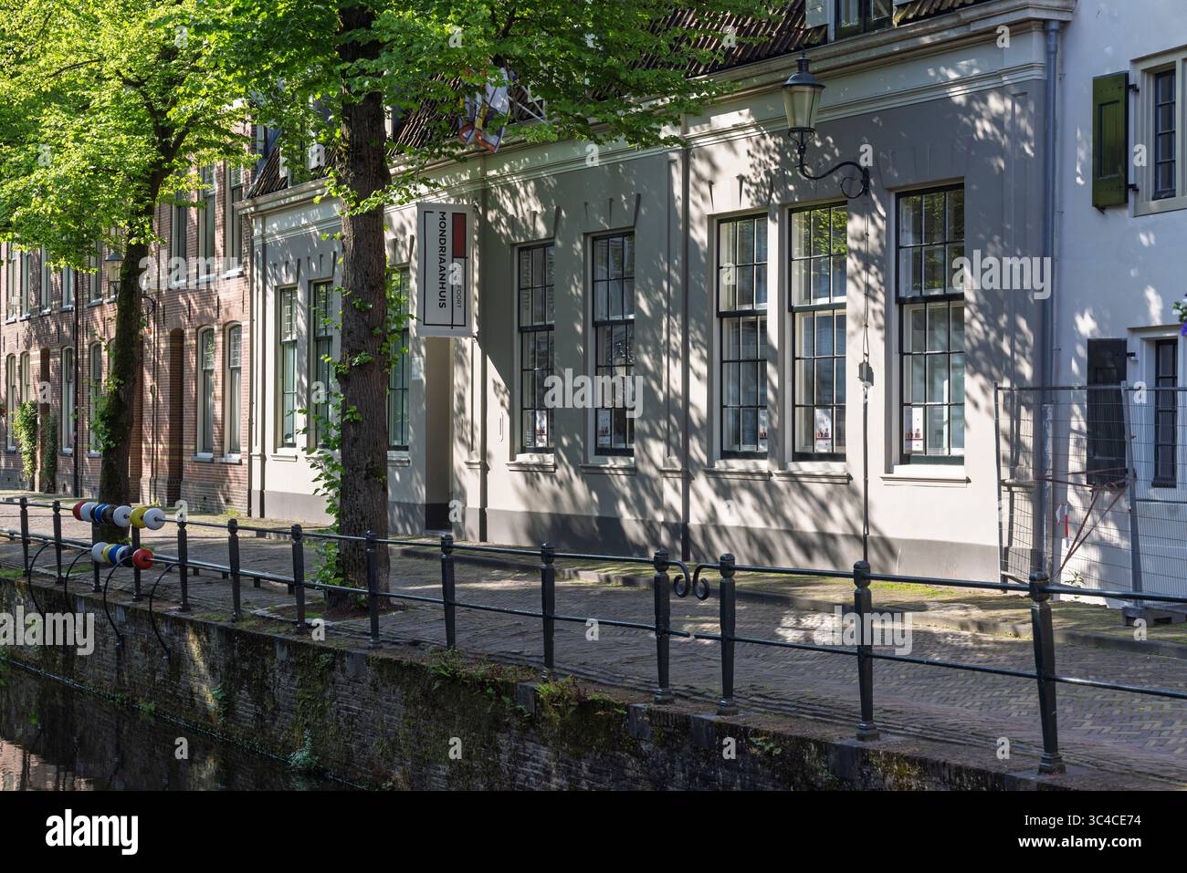 Eine ruhige Szene entlang eines niederländischen Kanals, mit dem Museum Mondriaanhuis, mit üppigen grünen Bäumen und traditioneller Architektur. Amersfoort, Niederlande, 1 Stockfoto