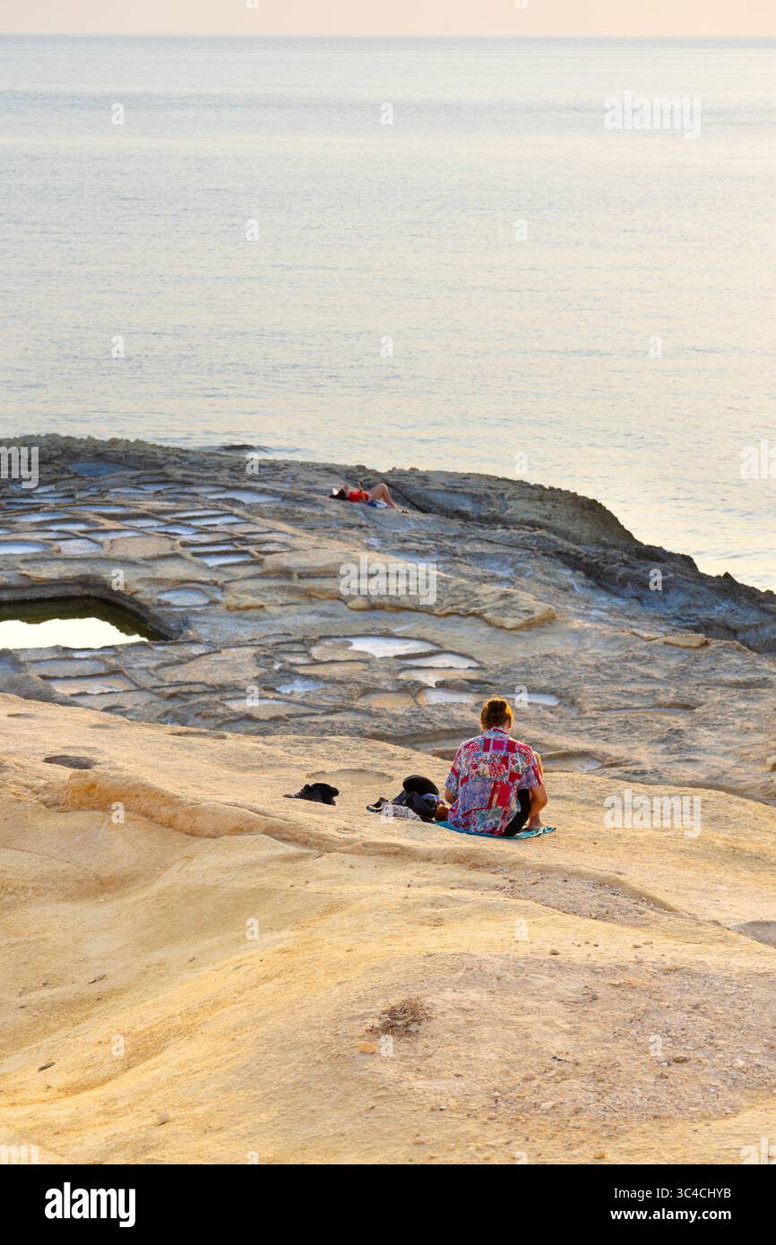 Menschen, die sich bei Sonnenuntergang an den Salinen am Xlendi Tower (Torri TAX-Xlendi), Xlendi Bay, Gozo, Malta entspannen Stockfoto