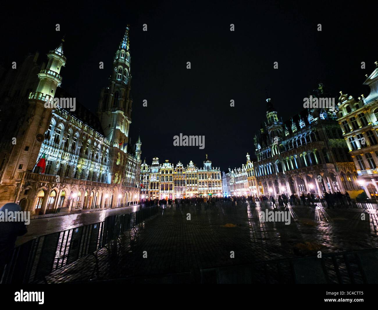 Nächtlicher Blick auf den beleuchteten Grand Place in Brüssel, Belgien, mit historischen Gebäuden und Menschenmassen auf dem Platz. - Smartphone-aufgenommenes Stockfoto