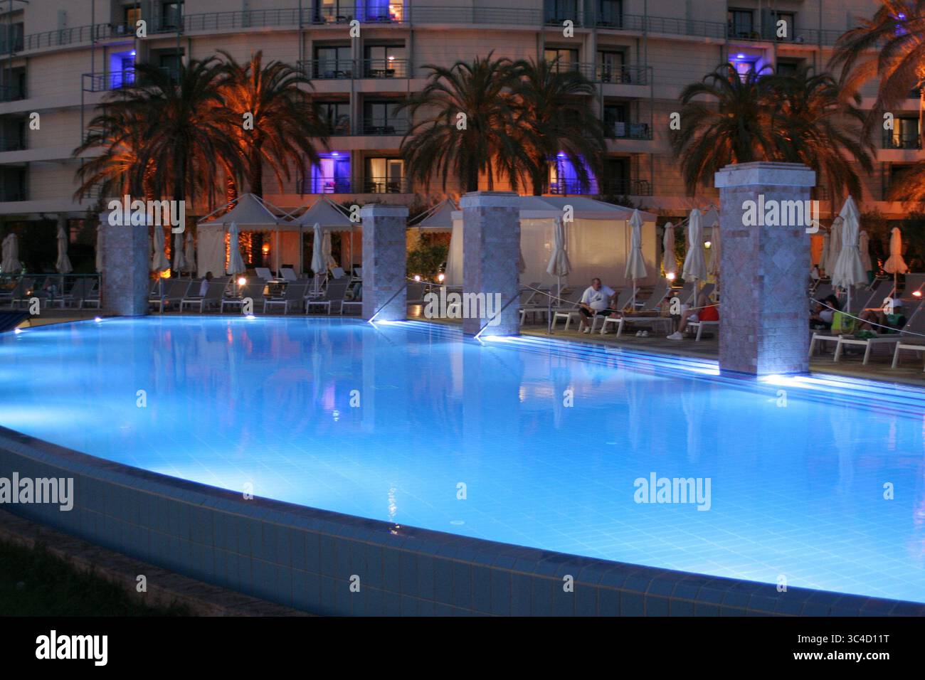 Atemberaubender Abendblick auf einen Pool mit blauem Licht, umgeben von Palmen und Hotelgebäuden. Stockfoto