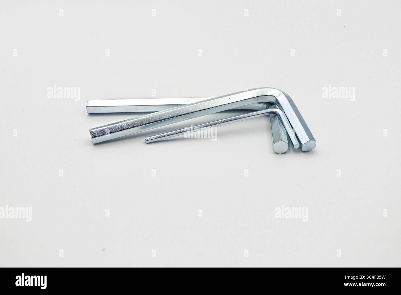 Drei L-förmige Innensechskantschlüssel in verschiedenen Größen aus Metall, die auf einer weißen Oberfläche angeordnet sind. Stockfoto