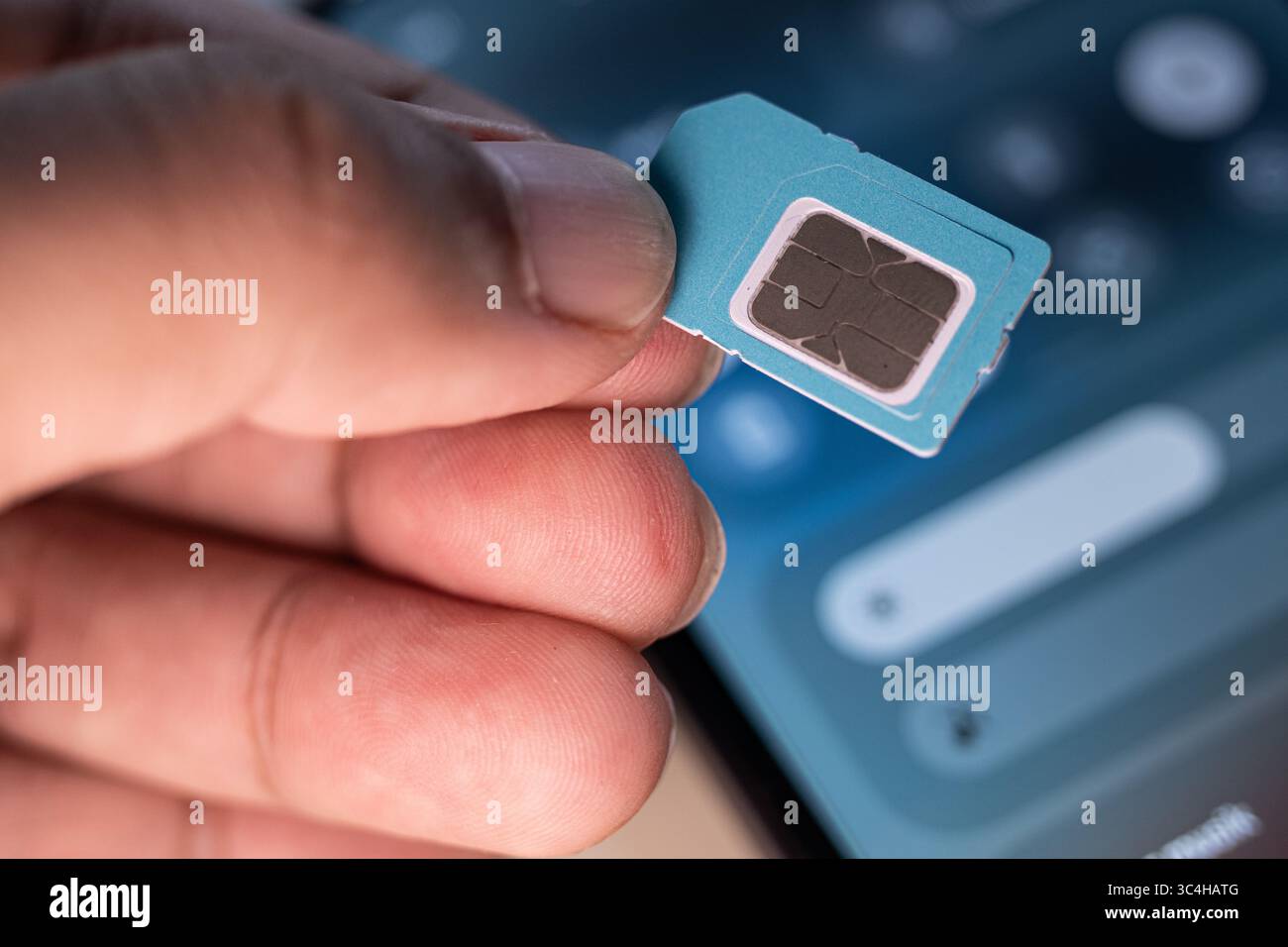 Hand hält eine SIM-Karte mit verschwommenem Smartphone im Hintergrund. Ideal für technische Tutorials, mobile Serviceangebote, Reparaturanleitungen oder Telekommunikation Stockfoto