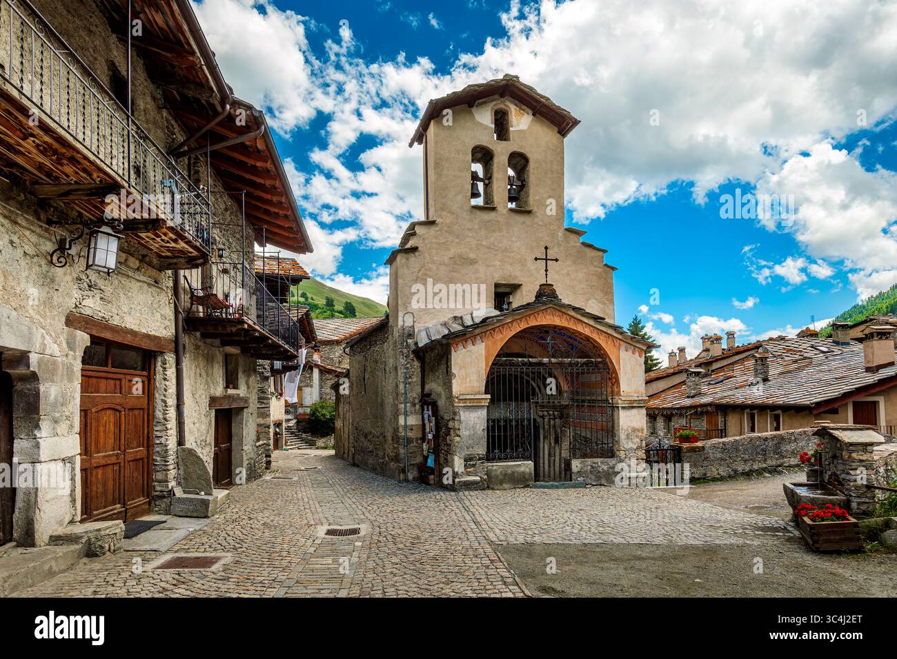 Ein malerischer Blick auf die Kopfsteinpflasterstraße zwischen alten traditionellen Steinhäusern und mittelalterlicher Kirche in Chianale, Italien. Stockfoto