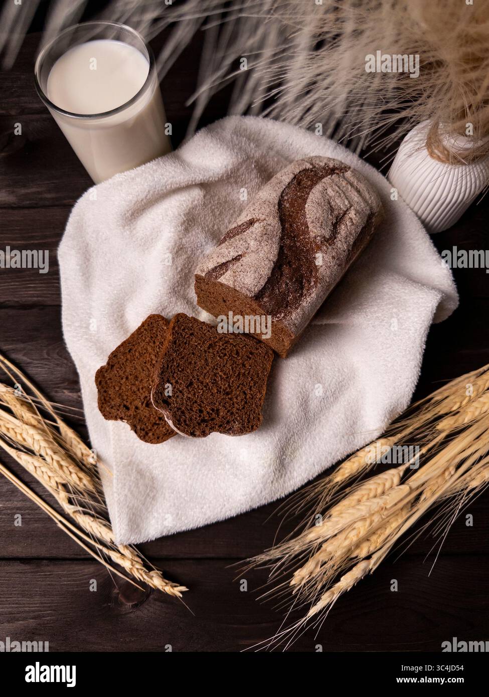 Ein gemütliches Stillleben mit dunklen Roggenbrotscheiben, einem Glas Milch und dekorativem Weizen für eine warme und einladende Atmosphäre Stockfoto