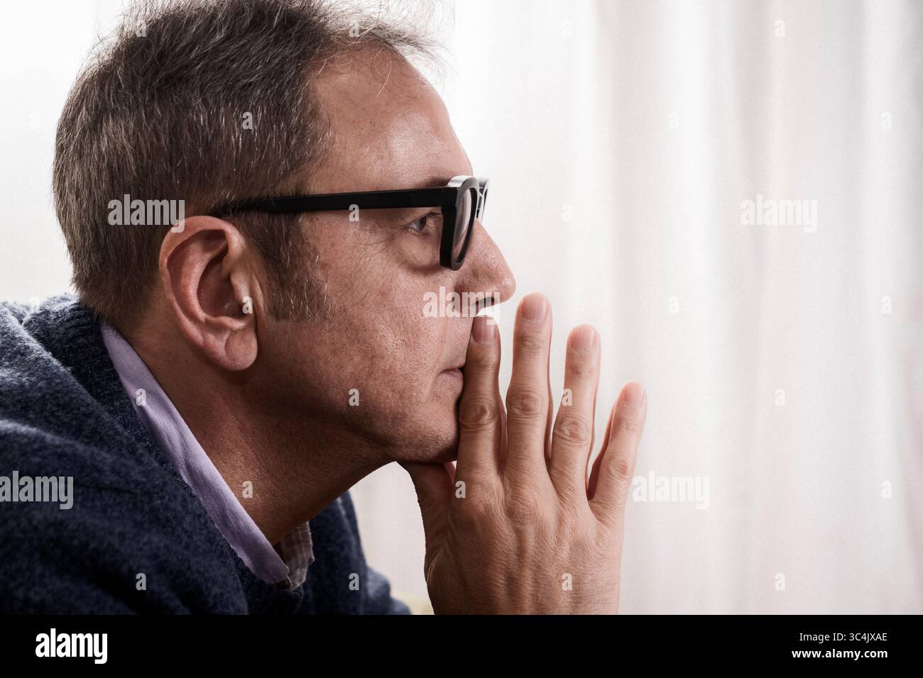 Introspektives Profilporträt eines ernsten Mannes mittleren Alters mit der Hand am Kinn, der eine schwierige Entscheidung erwägt oder unter Angst leidet. Stockfoto