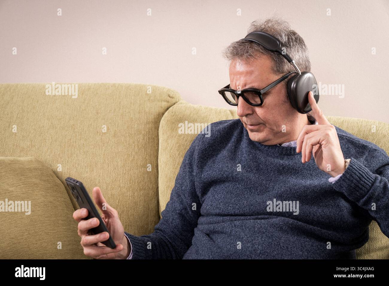 Reifer Mann mit geschlossenen Augen oder Blick nach unten, lauscht einer geführten Meditation oder beruhigender Musik auf Noise Cancelling-Kopfhörern, um Stress und anx zu reduzieren Stockfoto