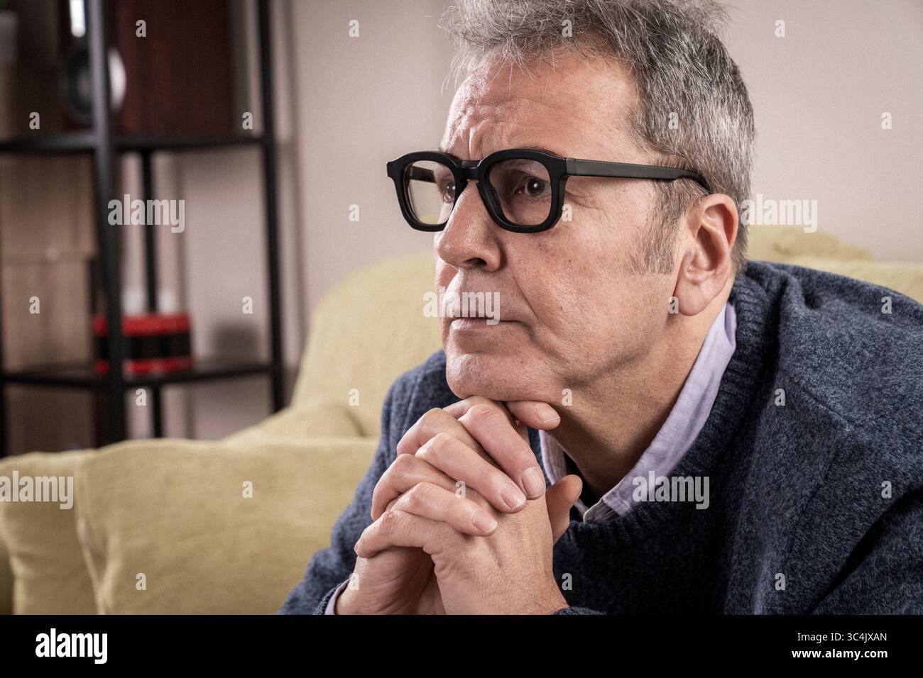 Nachdenklicher Mann mittleren Alters mit nachdenklichem Ausdruck und gefesselten Händen, der tief über eine persönliche Herausforderung oder eine Geschäftsstrategie nachdenkt. Stockfoto