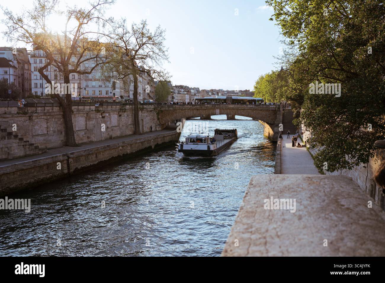 17-04-2025, Frankreich, Paris. Seine-Flussszene mit dem Sightseeing-Boot, das unter Pont Marie vorbeifährt. Die Leute laufen entlang der Uferpromenade. Klassisches Parisi Stockfoto