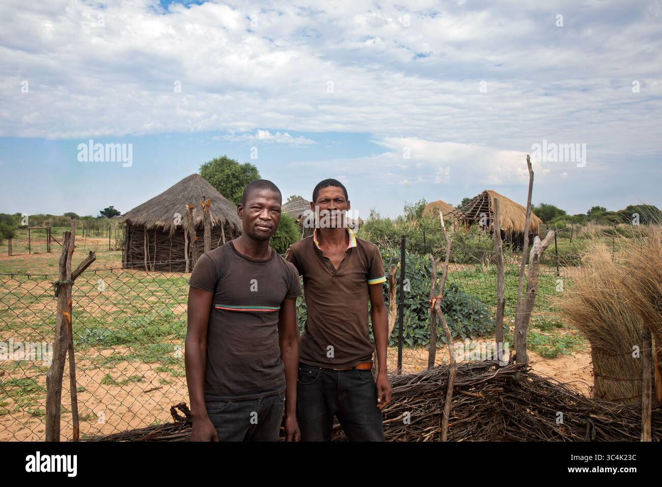 Afrikanisches Dorf, mit einem Porträt von zwei lächelnden afrikanischen Männern, die draußen stehen, mit einer Lehmhütte mit Strohdach im Hintergrund, die ländliche Umgebung einfangen Stockfoto