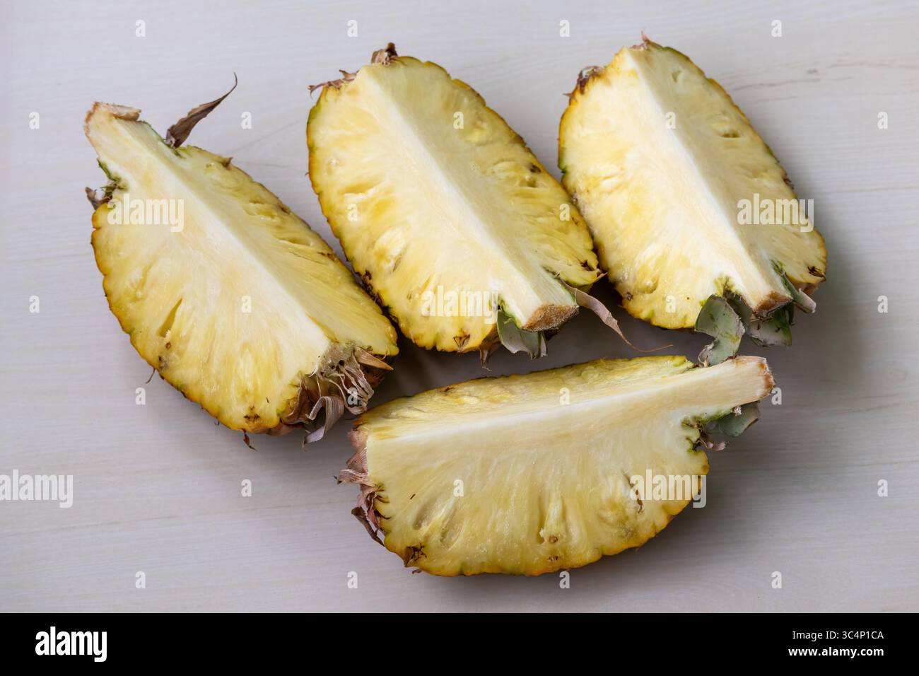 Reife Ananas, frisch in vier saftige Scheiben geschnitten, ruht auf hölzernem Hintergrund. Köstliche Ananas comosus Frucht für gesunde Ernährung und lebendiges Rezept Stockfoto
