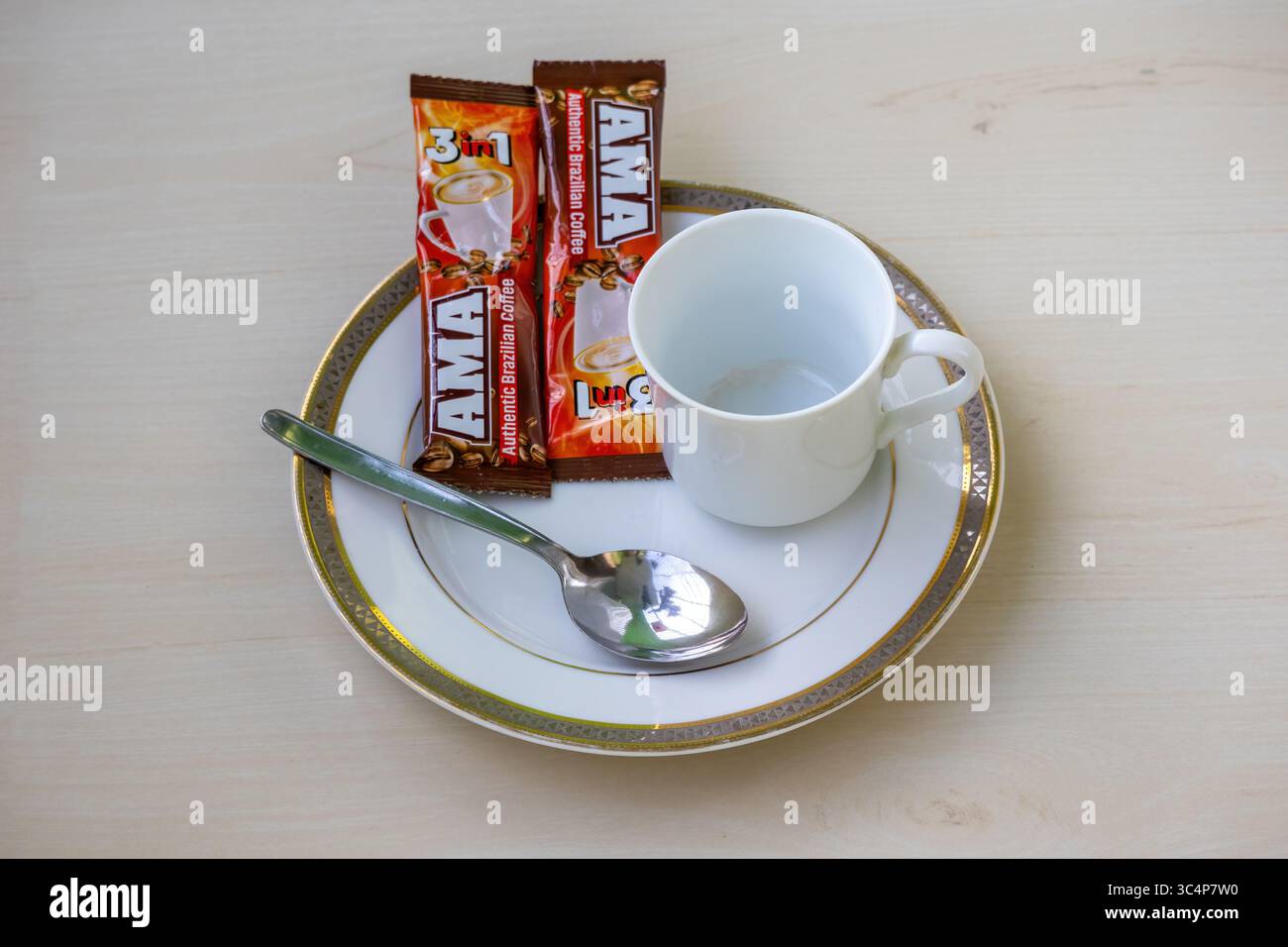 AMA Brasilianischer 3-in-1 Instant Coffee. Zwei 15-g-Beutel, leerer Becher und Löffel auf Keramikplatte. Authentischer Geschmack, bereit für einen schnellen und bequemen Cof Stockfoto