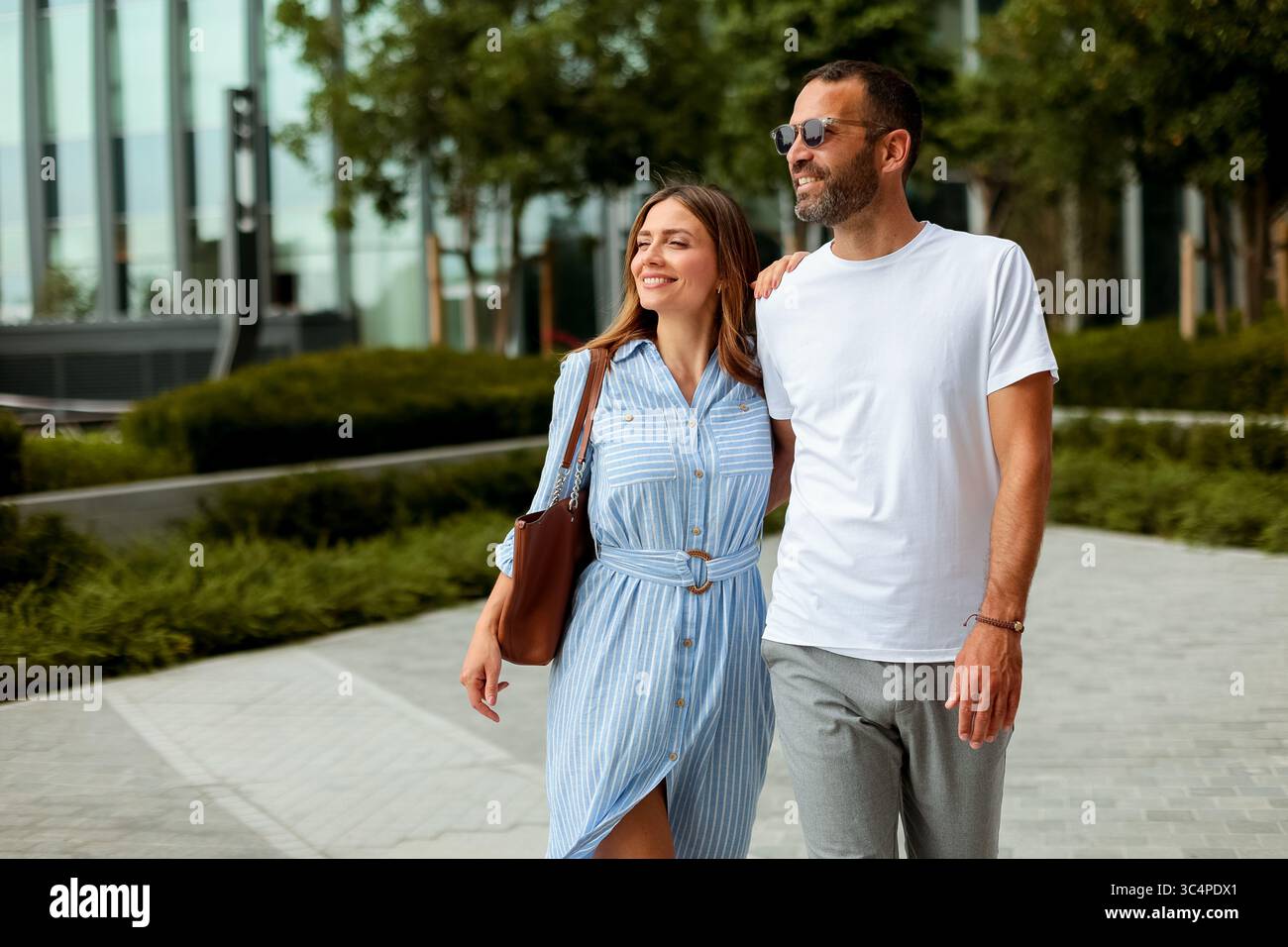 Zwei Personen spazieren friedlich in einem modernen Stadtpark, der Freude und Gesellschaft an einem hellen, sonnigen Tag widerspiegelt. Stockfoto
