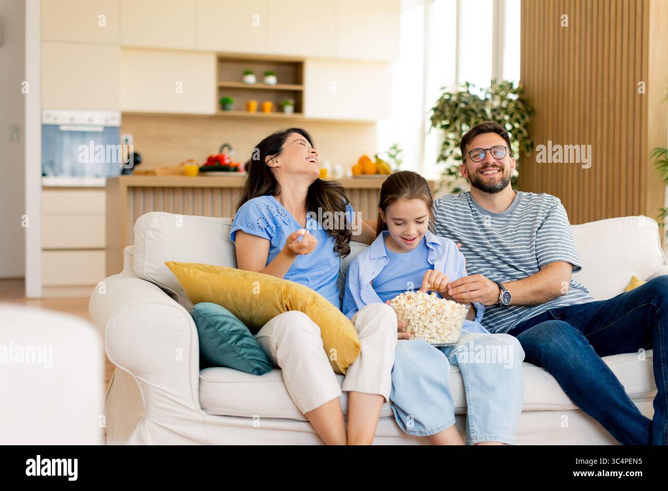 In einem warmen und einladenden Wohnzimmer teilt sich eine Familie eine Schüssel Popcorn, während sie zusammen in einem Film eine gute Zeit genießt. Stockfoto