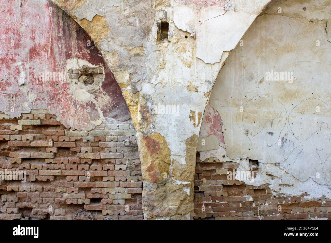 Nahaufnahme einer alten verwitterten Wand mit Schichten freiliegender Ziegelsteine, zerbröckeltem Putz und verblasster Farbe. Die Oberfläche zeigt Texturen und natürliche Farben Stockfoto
