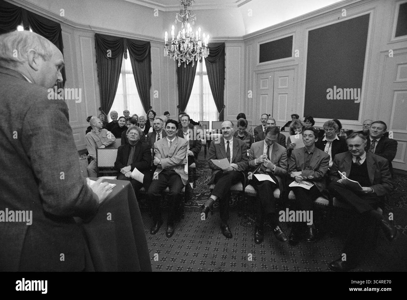 @@m.. Meeting Haarlem 2010, Haarlem, Dreef 3, Niederlande, 30-11-1998, Whizgle News, Dutch Desk, Niederlande, 1950-2000 Ein Redner spricht Ein breites Publikum in formeller Atmosphäre an, engagiert und aufmerksam. Die Teilnehmer zeigen eine Reihe von Ausdrucksformen, von konzentriertem Interesse bis hin zu nachdenklicher Betrachtung, während sie der Präsentation in einem elegant eingerichteten Raum mit Kronleuchtern und Vorhangfenstern zuhören. Stockfoto