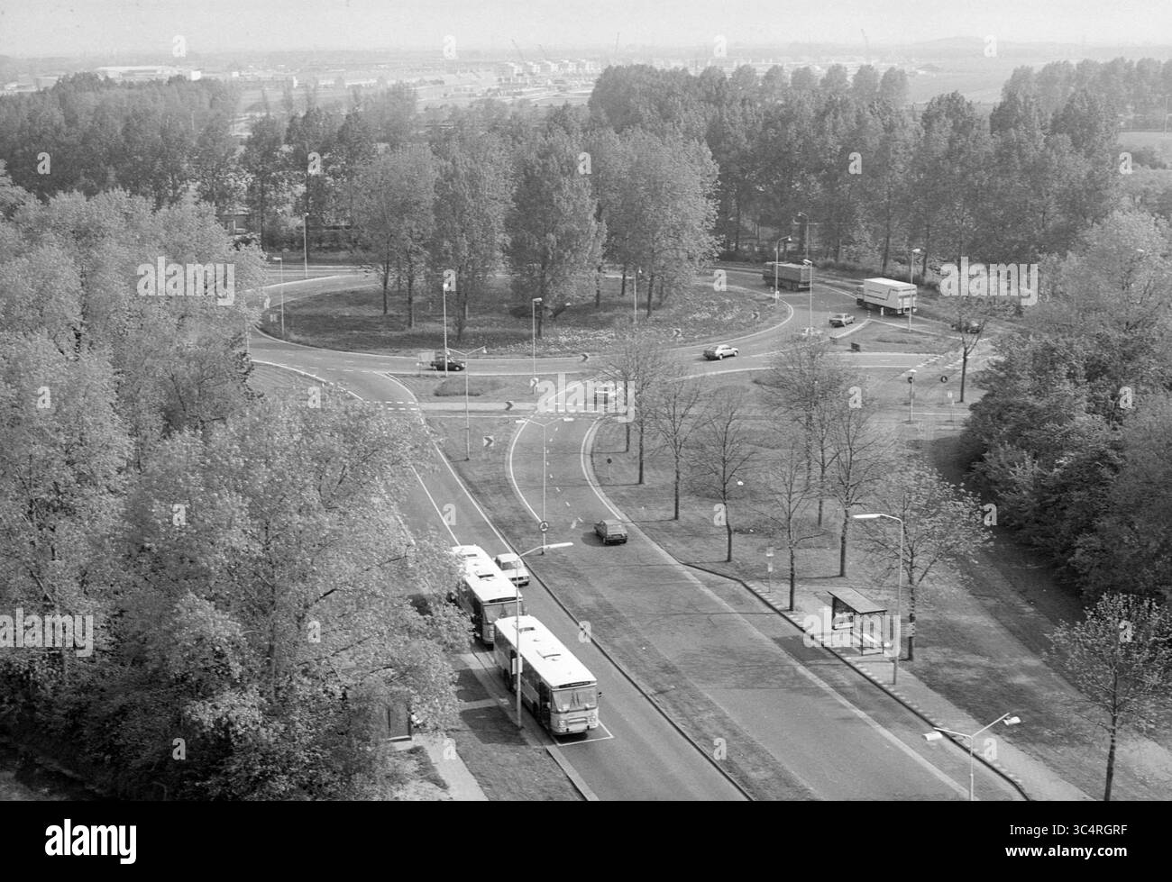 Delftplein aus 11 High Apartment, Pleinen, Haarlem, Delftplein, Niederlande, 16-05-1989 Whizgle News, Dutch Desk, Niederlande, 1950-2000 Ein geschäftiger Kreisverkehr ist von Bäumen umgeben, in dem Busse und Autos die Kreisstraße befahren. Verkehrszeichen und Beschilderungen sind sichtbar und zeigen den Fluss der Fahrzeuge an, während der Hintergrund entfernte Gebäude und mehr Grün zeigt. Stockfoto
