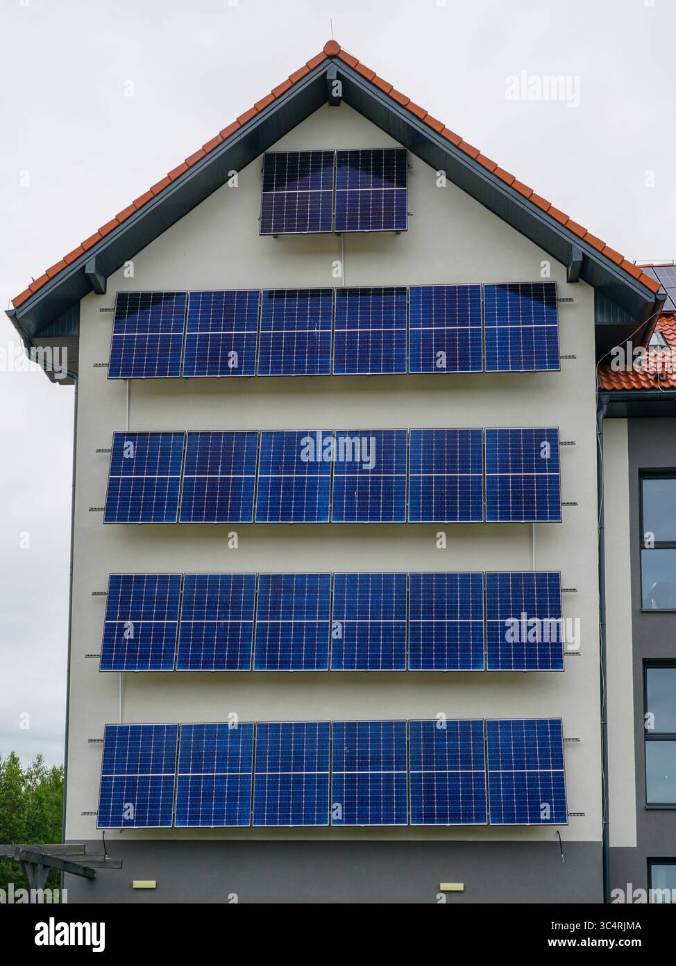 Ein modernes Gebäude mit mehreren Reihen blauer Solarpaneele an der Fassade, das vertikal energieeffizient gestaltet ist Stockfoto