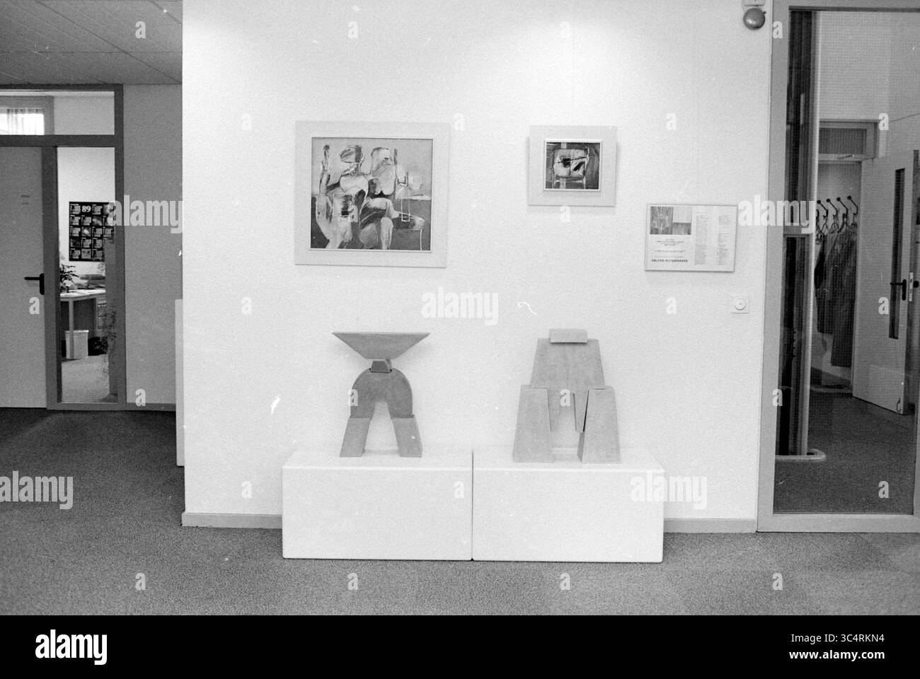 Ecke der Handelskammer mit Kunst, Handelskammer und Fabriken, 26-10-1989 Whizgle News, Dutch Desk, Niederlande, 1950-2000 Eine minimalistische Kunstausstellung zeigt zwei geometrische Skulpturen auf Sockeln, ergänzt durch gerahmte Kunstwerke an der Wand. Das Ambiente bietet einen modernen Galerieraum mit Schwerpunkt auf Einfachheit und künstlerischem Ausdruck. Stockfoto