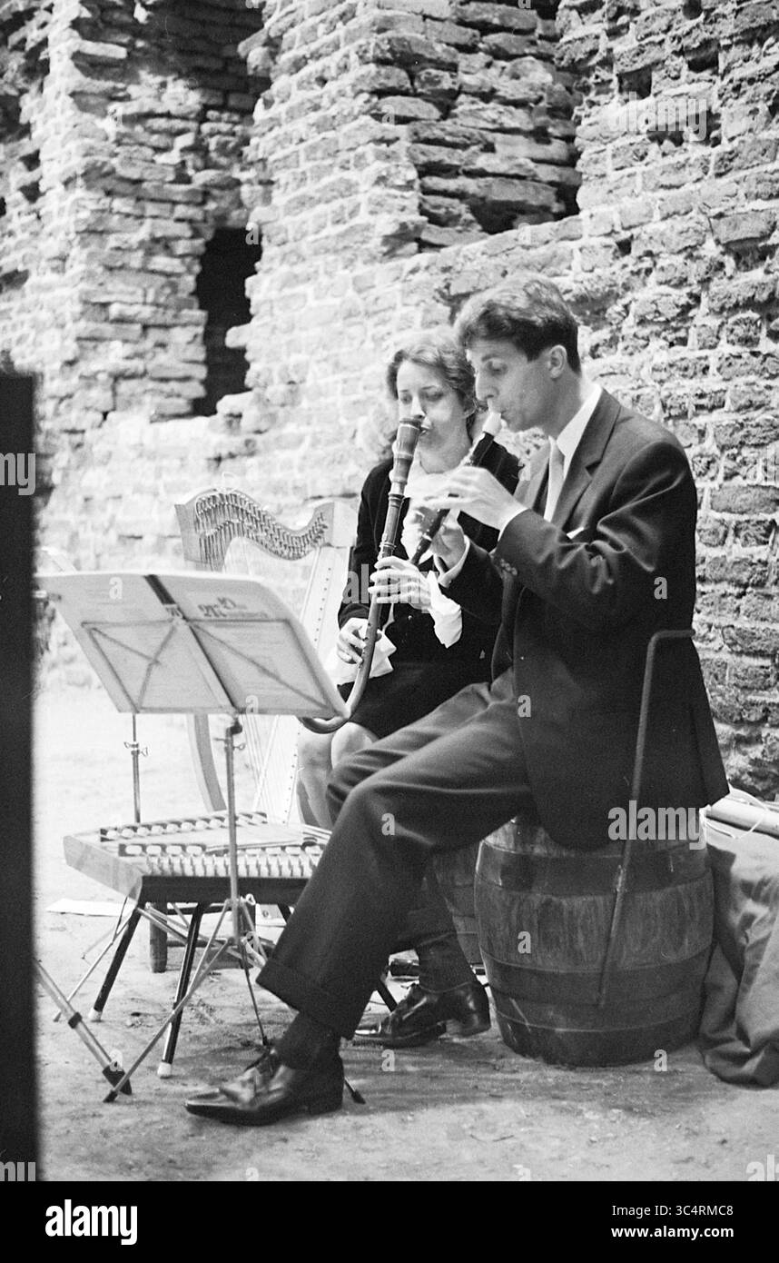 Ruine von Brederode mit Beleuchtung, Ruin, 20-05-1966 Whizgle News, Dutch Desk, Niederlande, 1950-2000 Ein Mann und eine Frau spielen Musik in einem rustikalen Ambiente, umgeben von alten Steinmauern. Der Mann spielt eine Holzflöte, während er auf einem Fass sitzt, und die Frau begleitet ihn mit einer Klarinette. Die Noten liegen auf einem Stand zwischen ihnen und schaffen eine ruhige Atmosphäre voller Melodien. Stockfoto