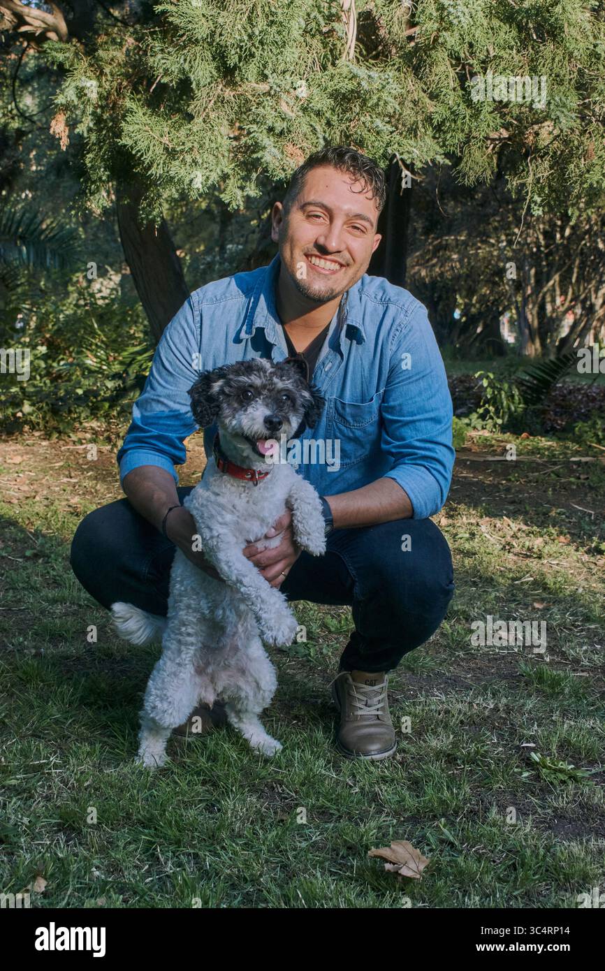 Der Mann hält liebevoll kleine schwarz-weiße Hunde in einem sonnigen Park, umgeben von Bäumen und Gras. Warmes Bild, das liebevolle Verbundenheit, Natur und Stockfoto