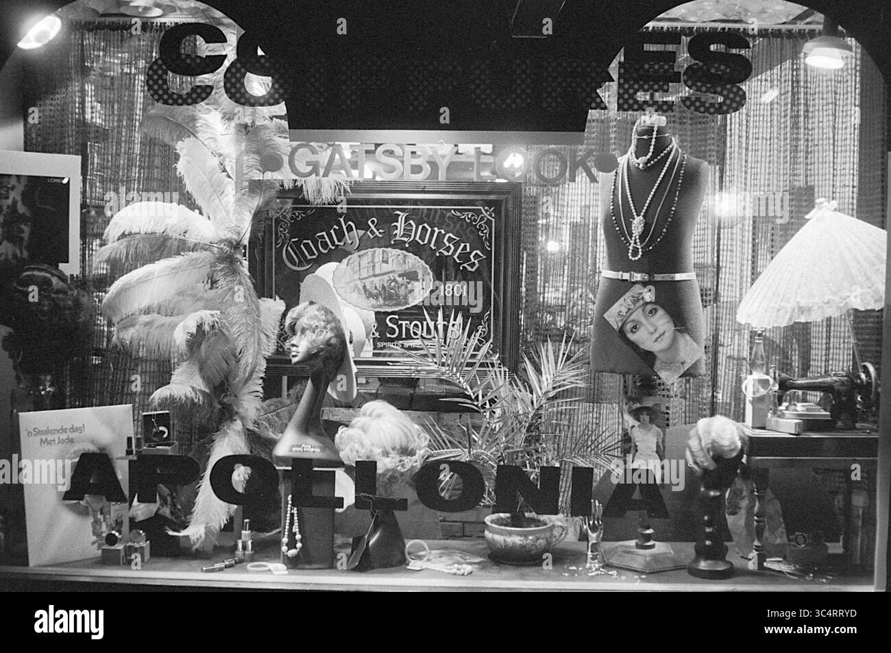 Salon Appolonia, Friseure und Friseursalons, 12-06-1974 Whizgle News, Dutch Desk, Niederlande, 1950-2000 Ein Vintage-Schaufenster zeigt eine eklektische Auswahl an Artikeln, darunter eleganter Schmuck, Federdekorationen und altmodische Accessoires. Die Szene fängt einen nostalgischen Charme mit einem Schild für „Coach & Horses“ und prominenten Schriften ein, die den Namen „Argelonia“ enthüllen. Verschiedene dekorative Stücke erinnern an Geschichte und Stil. Stockfoto