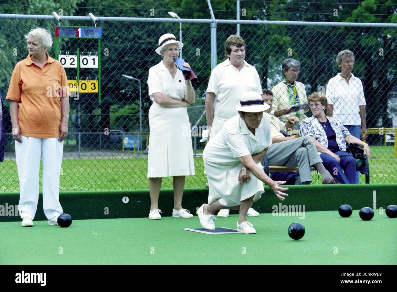 Bowls Ladies: Niederlande - England, 26-06-1999 Whizgle News, Dutch Desk, Niederlande, 1950-2000 Eine Gruppe von Frauen in koordinierten Outfits nimmt an einem Rasenbowlingspiel Teil, bei dem ein Spieler in Aktion ist, der den Ball auf das Ziel zurollen will. Die Zuschauer beobachten von der Seitenlinie aus, während eine Anzeigetafel die Punktzahl im Hintergrund anzeigt. Stockfoto