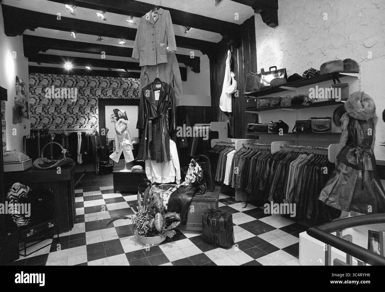 Intr. Ledergeschäft Grote Markt, Haarlem, Grote Markt, Niederlande, 23-11-1973 Whizgle News, Dutch Desk, Niederlande, 1950-2000 Eine Boutique-Inneneinrichtung bietet elegant angeordnete Kleidung und Accessoires mit einer Vielzahl von stilvollen Mänteln, Taschen und Hüten. Das einzigartige Dekor umfasst gemusterte Tapeten und warme Beleuchtung, die eine gemütliche Shopping-Atmosphäre schaffen. Ein zentrales Display sorgt mit einem auffälligen Outfit, das gut sichtbar drapiert ist. Stockfoto