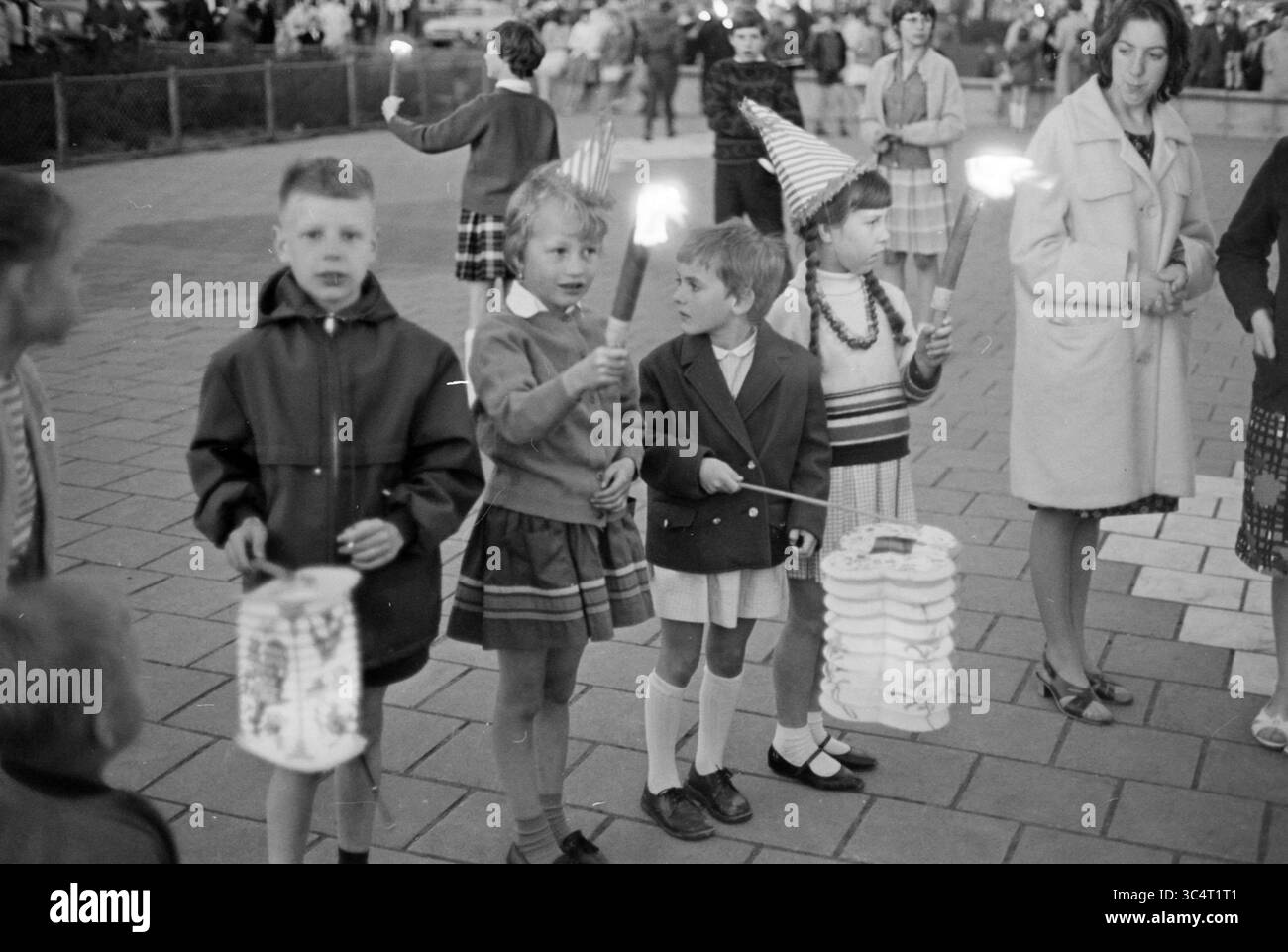 Laternen Parade Whizgle News, Dutch Desk, Niederlande, 1950-2000 Eine Gruppe von Kindern feiert mit Laternen, Funkeln und festlichen Hüten, während Erwachsene in der Nähe zusehen und eine fröhliche und lebhafte Atmosphäre schaffen. Stockfoto
