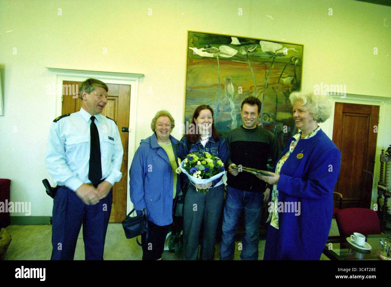 Lob Mr. Huissen, Heemstede, Heemstede, Niederlande, 25-04-2000 Whizgle News, Dutch Desk, Niederlande, 1950-2000 Eine Gruppe von vier Personen steht zusammen und lächelt herzlich. Einer trägt eine Polizeiuniform, während der andere einen Blumenstrauß hält. Die Kulisse zeigt ein farbenfrohes Gemälde an der Wand, und es gibt ein Gefühl von Feier und Kameradschaft in der Gruppe. Stockfoto