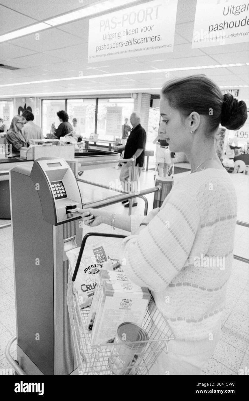 Selbstscan-Kasse, Albert Heijn, Heemstede, Heemstede, Niederlande, 10-07-1994 Whizgle News, Dutch Desk, Niederlande, 1950-2000 Ein Käufer steht an einer Selbstkasse und scannt Artikel aus einem mit Lebensmitteln gefüllten Korb. Die Szene fängt eine geschäftige Supermarktatmosphäre mit anderen Kunden im Hintergrund ein. Helle Beschilderung gibt den Bereich an, der für Self-Service-Checkouts vorgesehen ist. Stockfoto